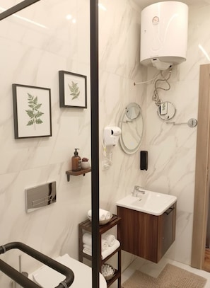 Un baño moderno con pared de mármol, un lavamanos, un espejo, un perchero para toallas y una ducha con cabezal de ducha de mano.
