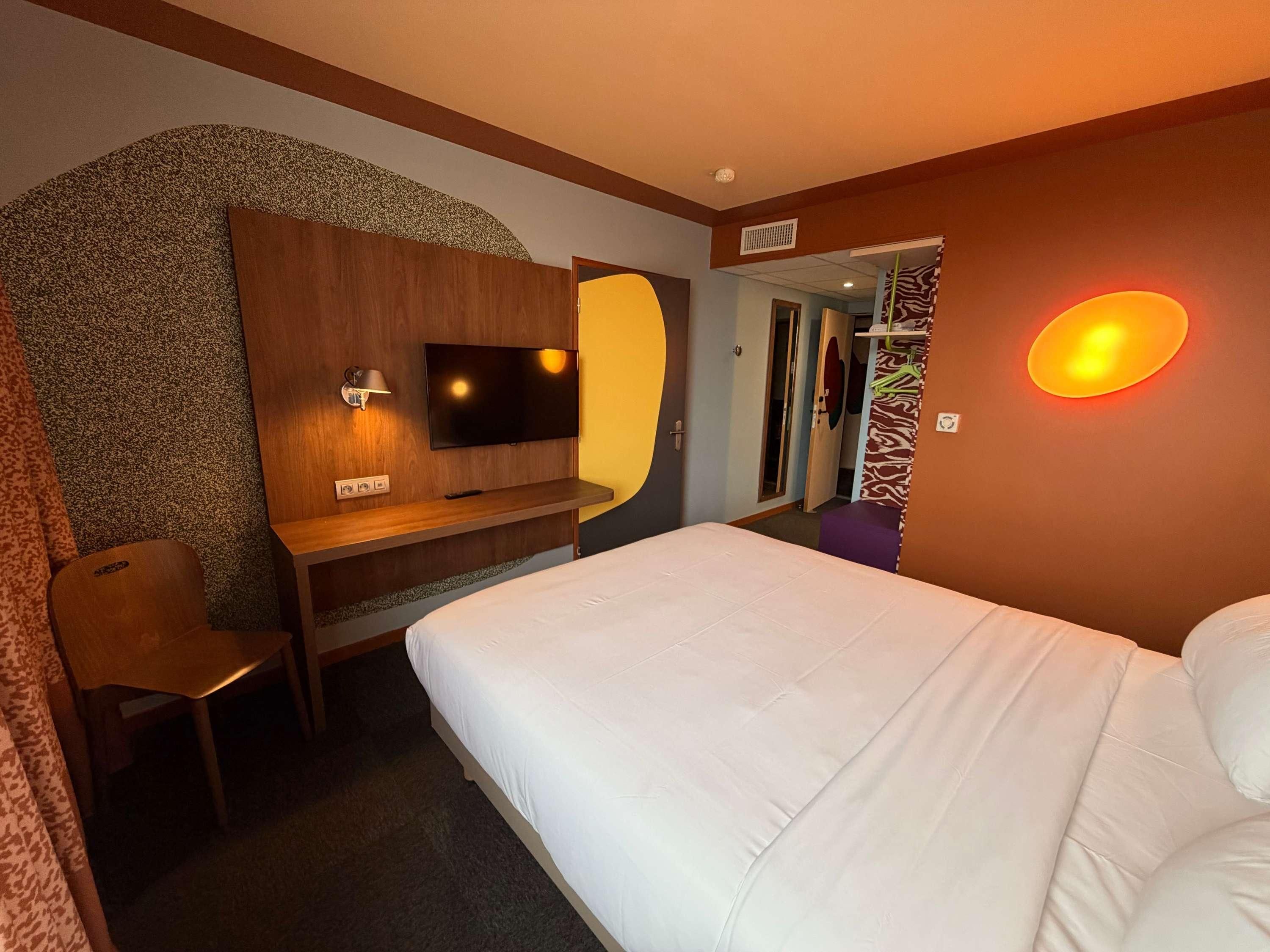 Una habitación de hotel con cama, escritorio con televisor, espejo y zona de ducha.