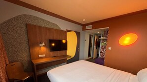 A hotel room with a bed, a desk with a TV, a mirror, and a shower area. - Ibis Styles Ales Centre Cevennes (Ales)