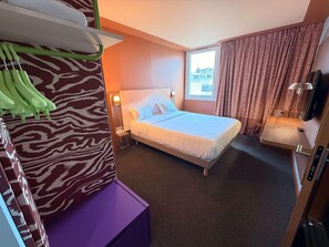 A hotel room with a bed, a desk, a chair, a window with curtains, a wall-mounted TV, and a zebra-patterned wall. - Ibis Styles Ales Centre Cevennes (Ales)