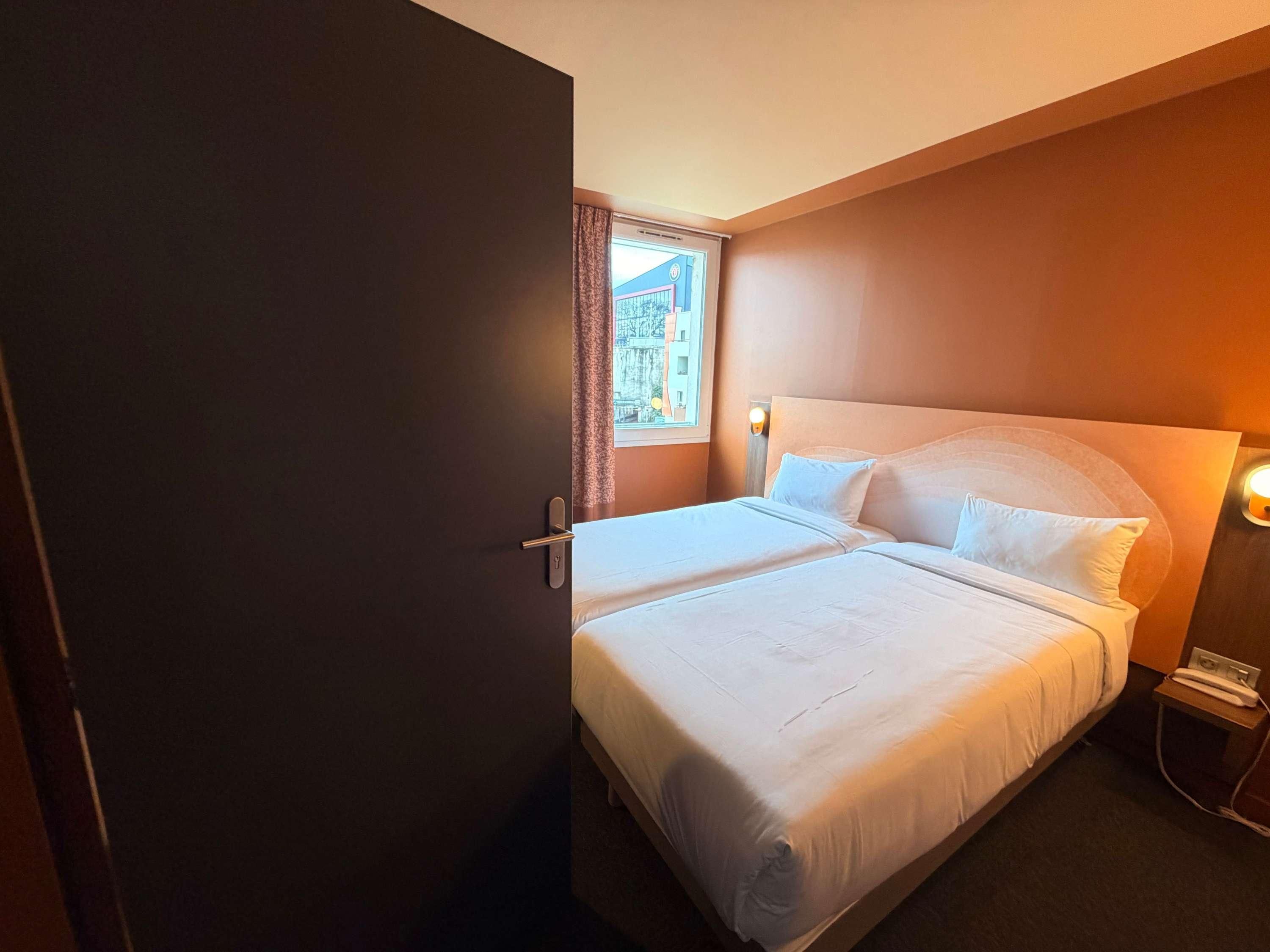 Een hotelkamer met een bed, nachtkastje, lamp en een raam met gordijnen.
