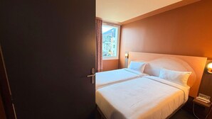 A hotel room with a bed, a nightstand, a lamp, and a window with curtains. - Ibis Styles Ales Centre Cevennes (Ales)