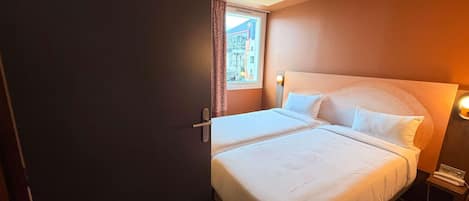 A hotel room with a bed, a nightstand, a lamp, and a window with curtains.