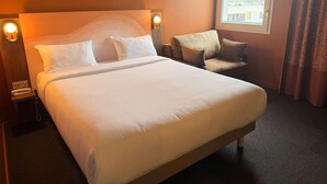 A hotel room with a large bed, a sofa, a bedside table with a lamp, and a window with curtains. - Ibis Styles Ales Centre Cevennes (Ales)
