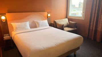 Ein Hotelzimmer mit einem großen Bett, einem Sofa, einem Nachttisch mit Lampe und einem Vorhangfenster.