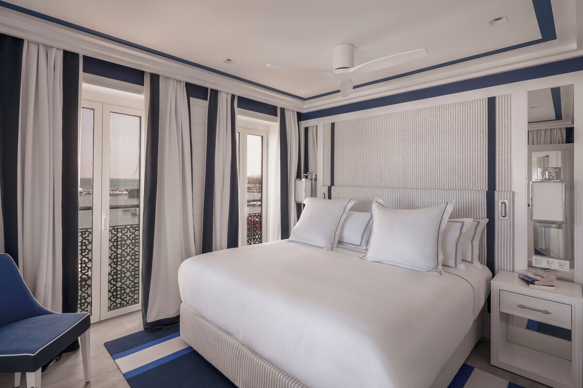 Une chambre d’hôtel avec un grand lit, une table de chevet, une chaise et une vue sur la mer par la fenêtre.