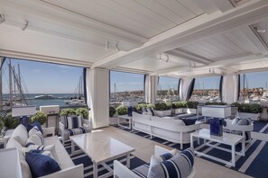 A spacious outdoor seating area with white furniture and blue accents, overlooking a marina with boats. - MIM Sotogrande Member of Meliá Collection (Cadiz)