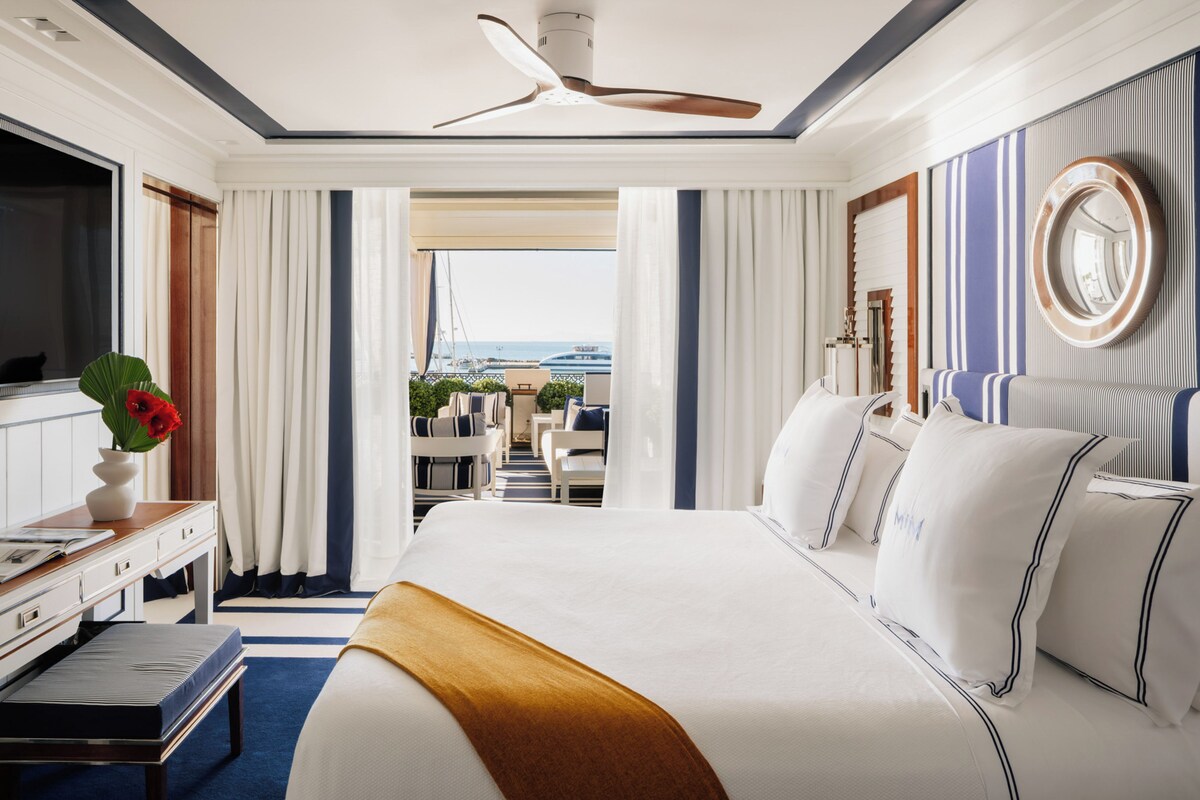 Une chambre d’hôtel avec un grand lit, un bureau avec un ordinateur, une télévision et une vue sur l’océan.