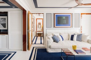 A modern bedroom with a white sofa, blue and white pillows, a blue and white striped rug, and a ceiling fan. - MIM Sotogrande Member of Meliá Collection (Cadiz)
