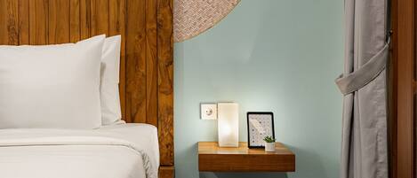 A neatly made bed with white linens, a wooden headboard, a small wooden nightstand with a lamp, a framed picture, and a small plant.