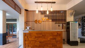 A reception area with a wooden reception desk, a refrigerator, and a fan. - Cove Asanaya (Canggu)