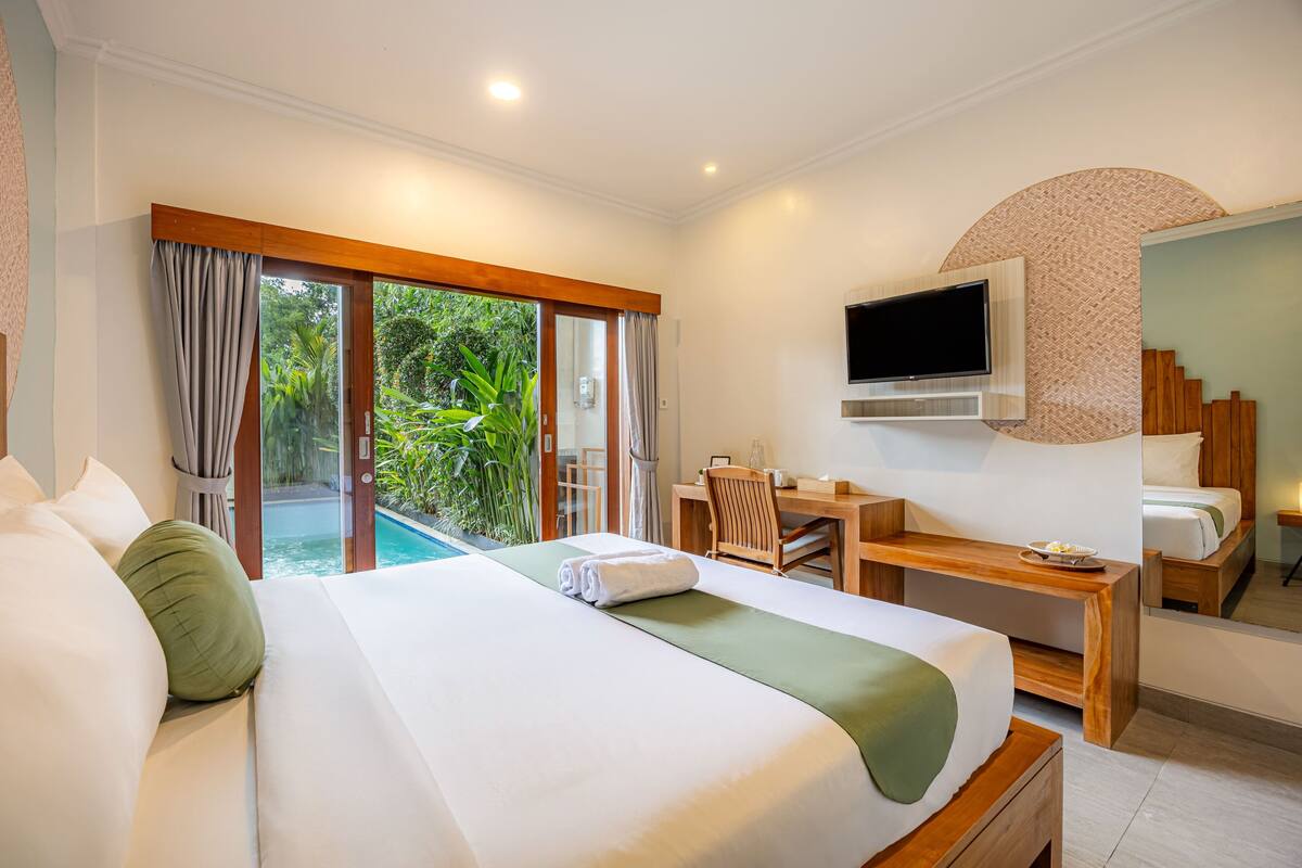 Une chambre d’hôtel dotée d’un grand lit, d’un bureau, d’un téléviseur à écran plat et d’une porte-fenêtre coulissante donnant sur une zone avec piscine.