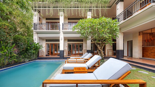 A poolside area with lounge chairs and a tree. - Cove Asanaya (Canggu)