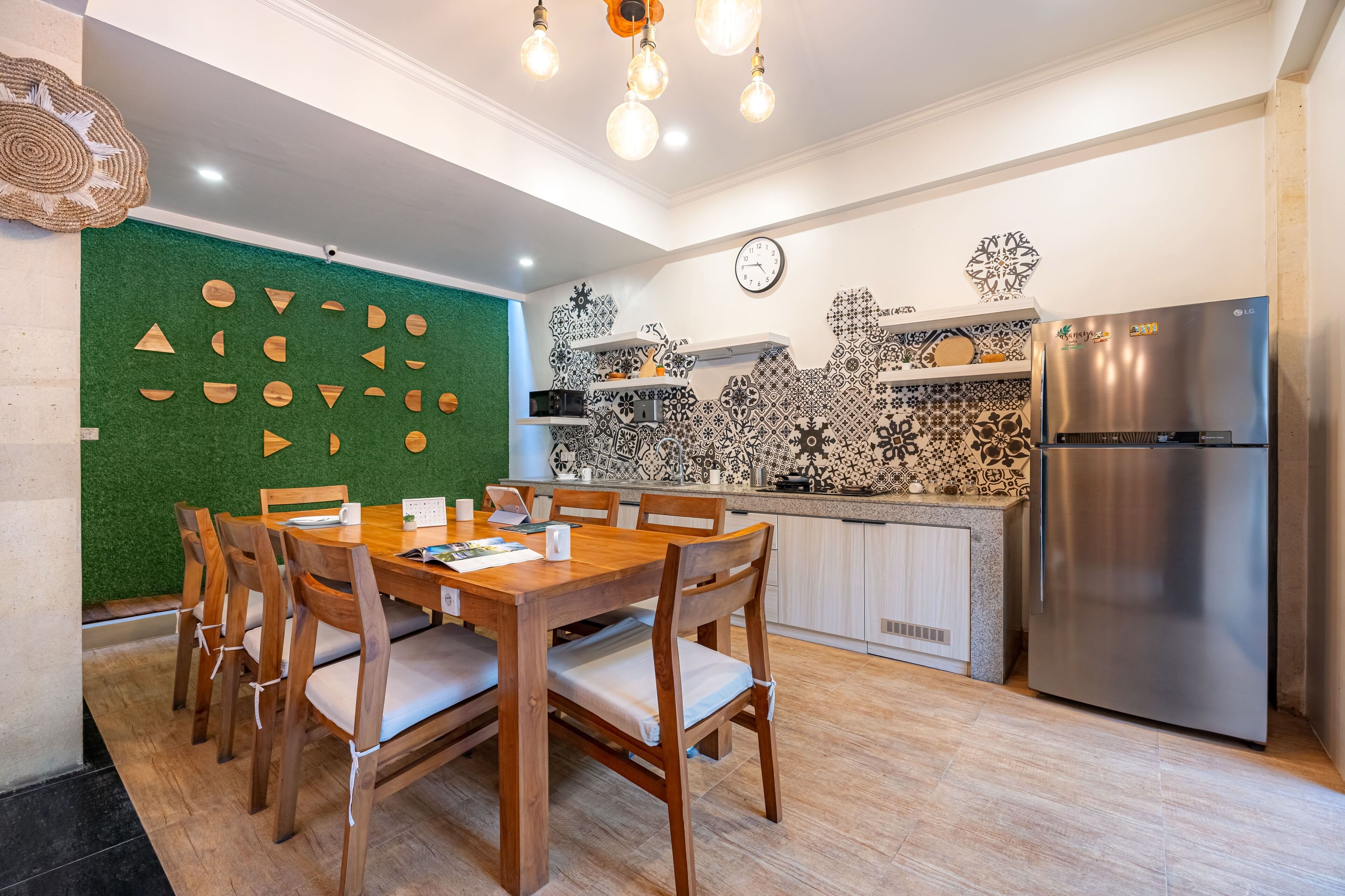 Una cocina moderna con comedor, que presenta una pared verde con formas geométricas, un refrigerador de acero inoxidable y un salpicadero de azulejos.