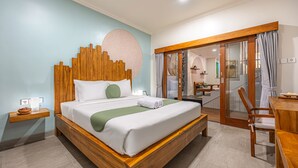 A modern hotel room with a wooden bed, a green throw, and a view of the dining area through a glass door. - Cove Asanaya (Canggu)