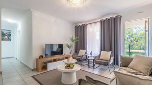 Ein modernes Wohnzimmer mit Flachbildfernseher, Couchtisch mit Dekoration, einer Couch und einem Sessel.