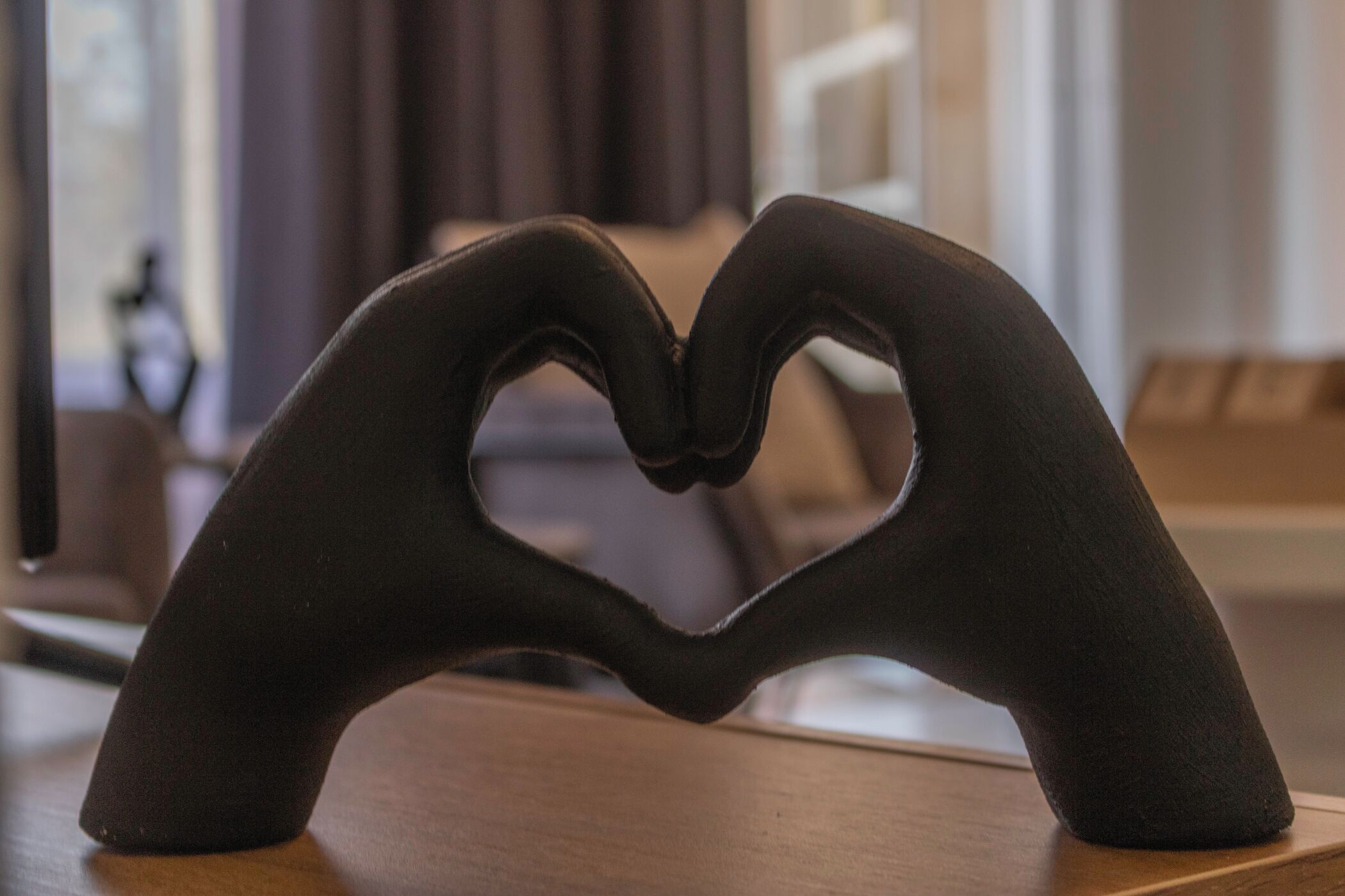 Um objeto em formato de coração feito de material preto, possivelmente uma escultura, colocado sobre uma superfície de madeira.