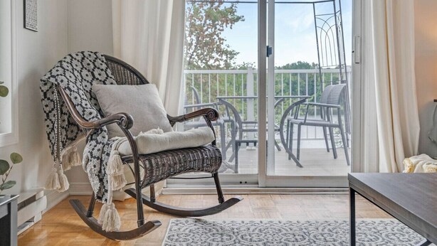 Et hyggeligt værelse med en gyngestol og en stor skydedør, der fører ud til en balkon med stole.