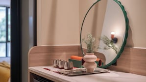 A bathroom with a mirror, a sink, a trash bin, and a small potted plant. - LILYBETH HOTEL PRATUNAM (Bangkok)