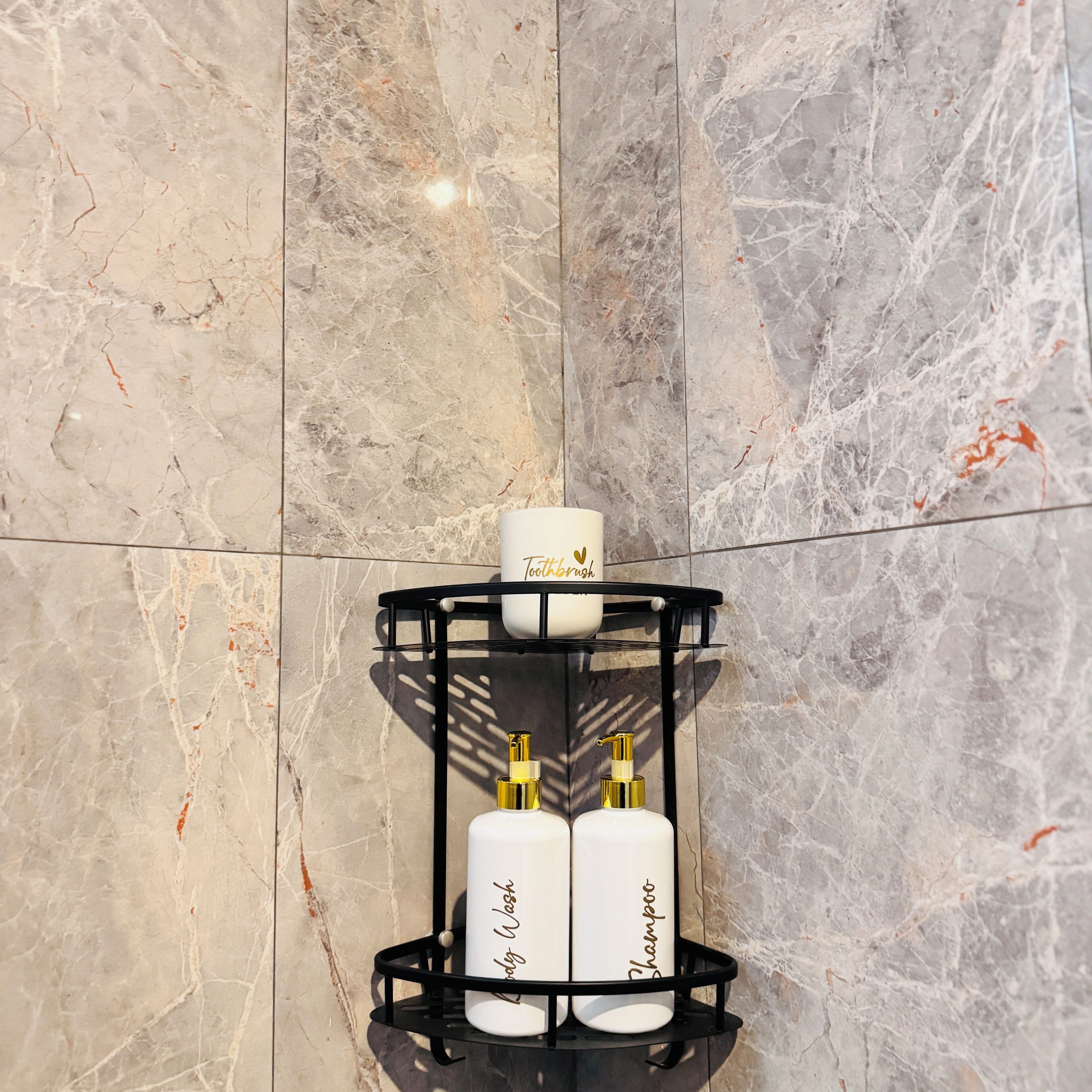 A bathroom with a marble wall and a black metal shelf holding toiletries.