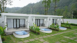 A modern building with a pool area, outdoor seating, and a view of a forested hillside.