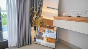 A modern bathroom with a large mirror, a wooden vanity, and a view of a bedroom with a bed and a window.