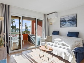 A hotel room with a balcony, a bed, a table with a bottle and glass, and a painting on the wall. - Apt, sea view, 50 m from the beach, A/C (Les Issambres)