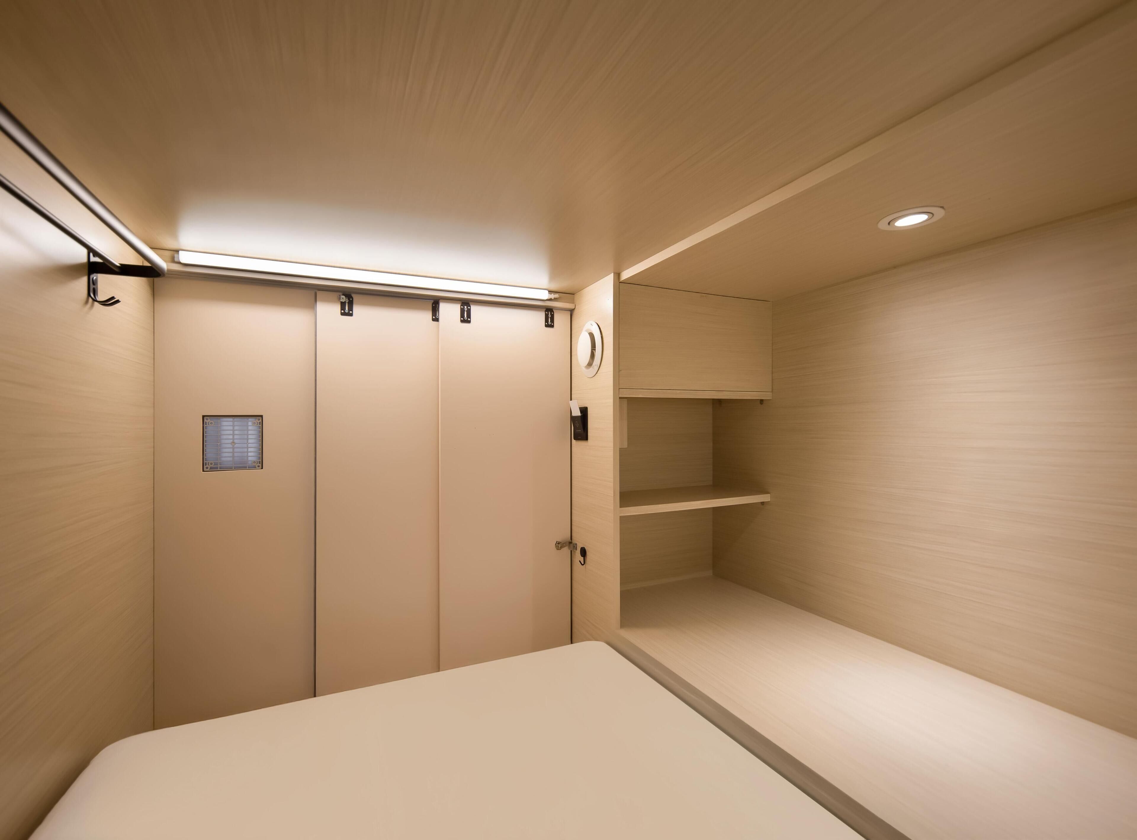 Una habitación minimalista con una cama, un estante pequeño y una puerta con picaporte.