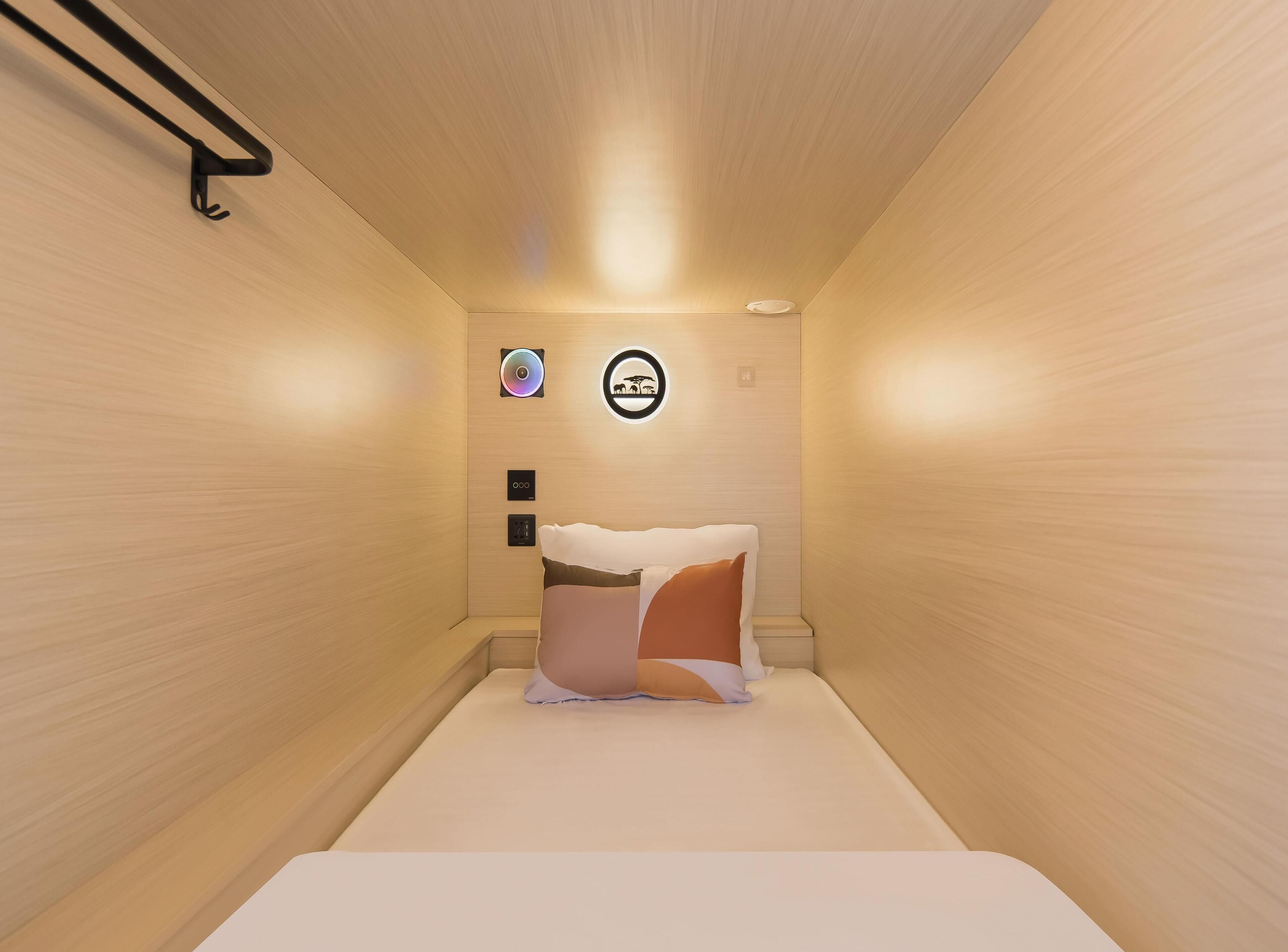 A small, cozy room with a bed, a wall-mounted light, and a circular decoration.