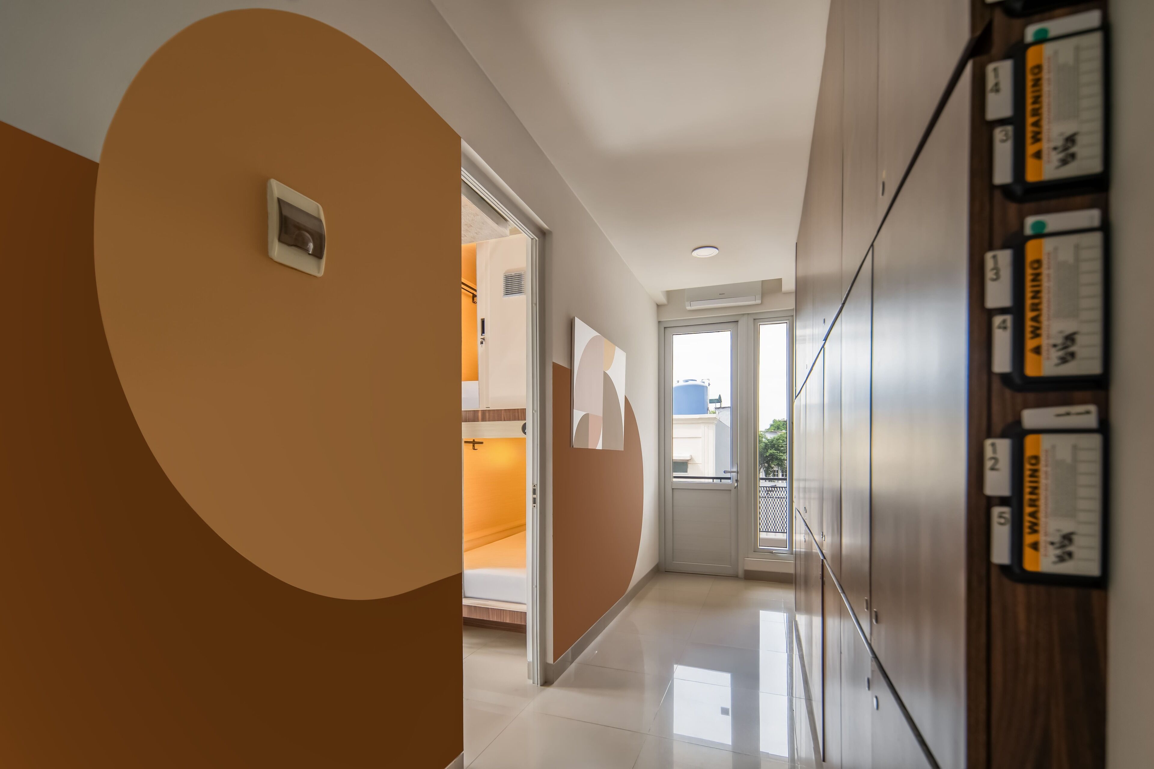 Ein moderner Hotelkorridor mit großem, kreisförmigen Wanddekor, einer zur Zimmerführenden Tür und einem an der Wand befestigten Warnschild.