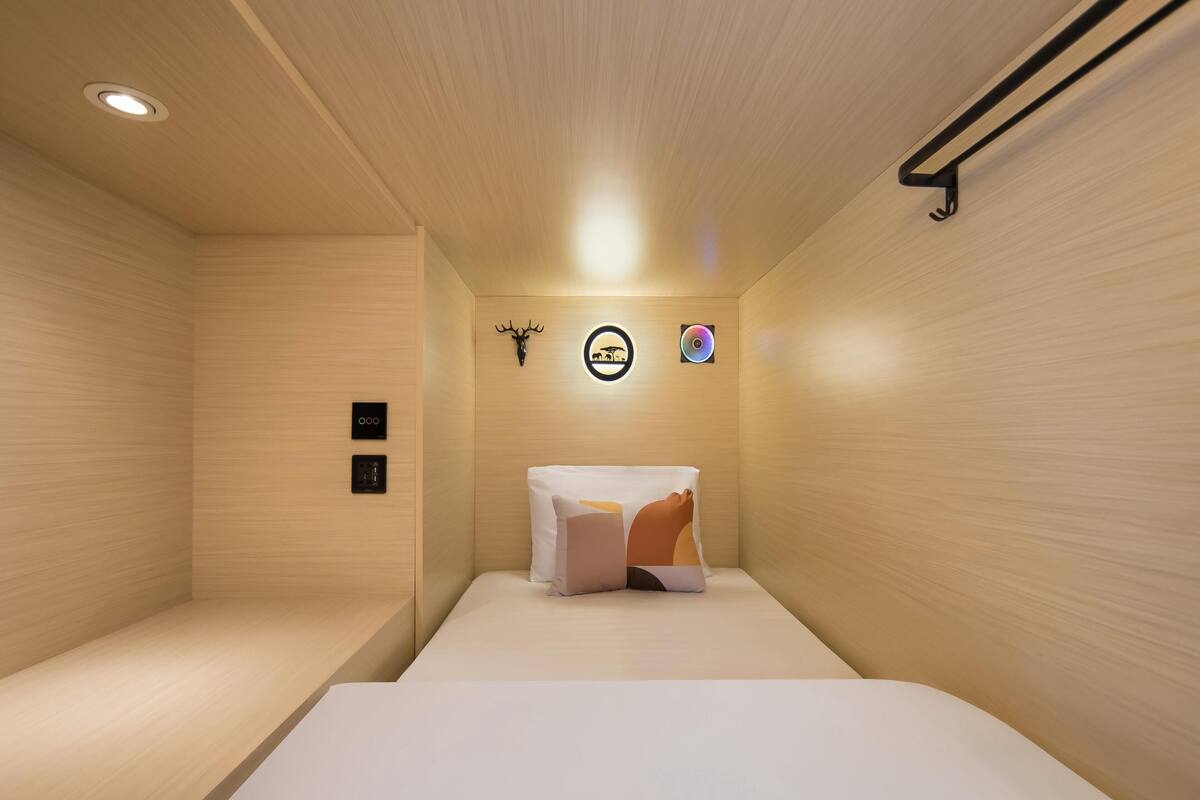 Een minimalistisch ingerichte kamer met een bed, een plafondlamp, een wandventilator en een decoratief hertenhoofd.