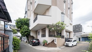 Un edificio residencial de varios pisos con un vestíbulo cubierto, una escalera que conduce a la entrada y un estacionamiento con dos automóviles.