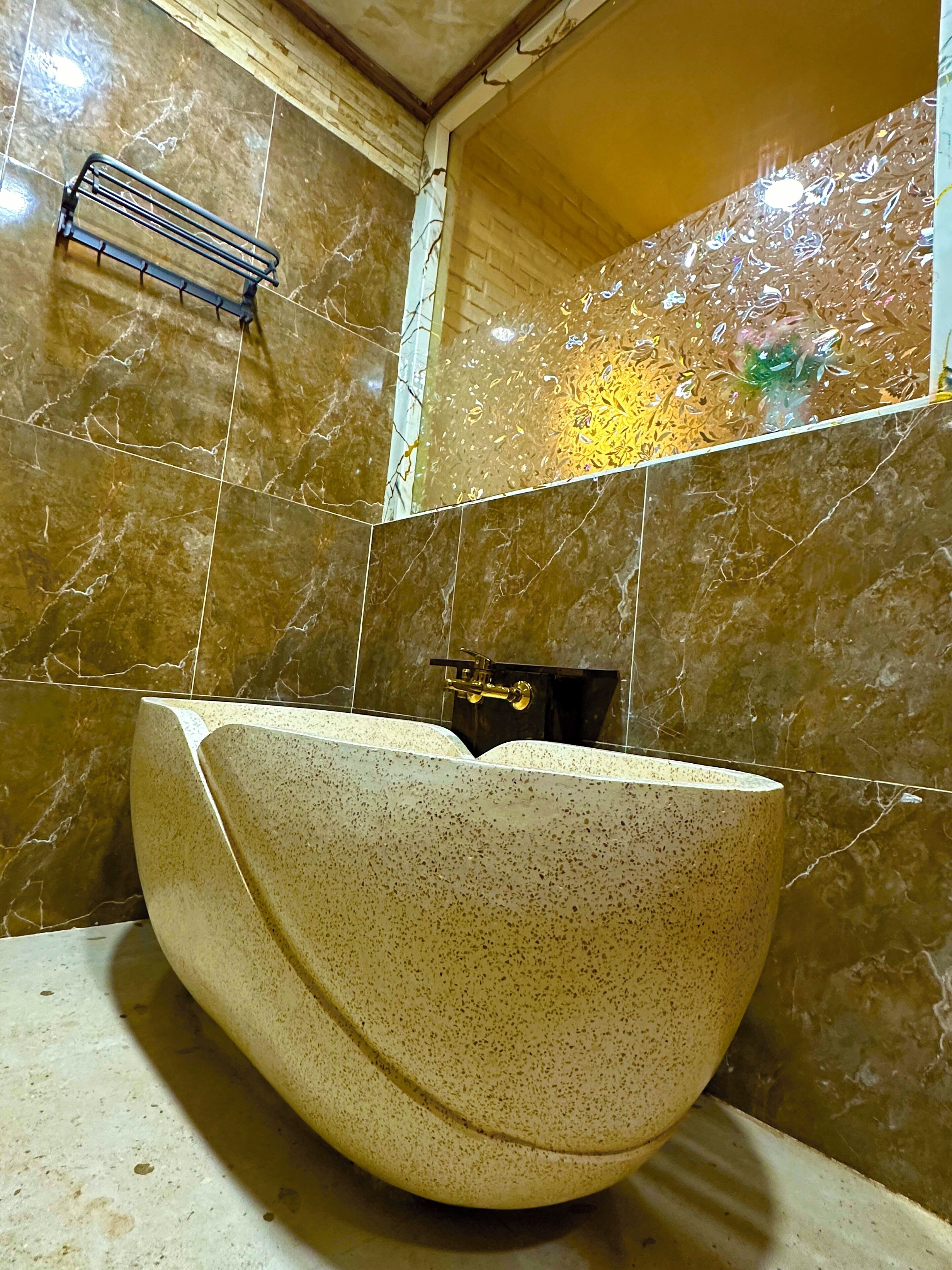 A bathroom with a large, bowl-shaped sink, tiled walls, and a small shelf.