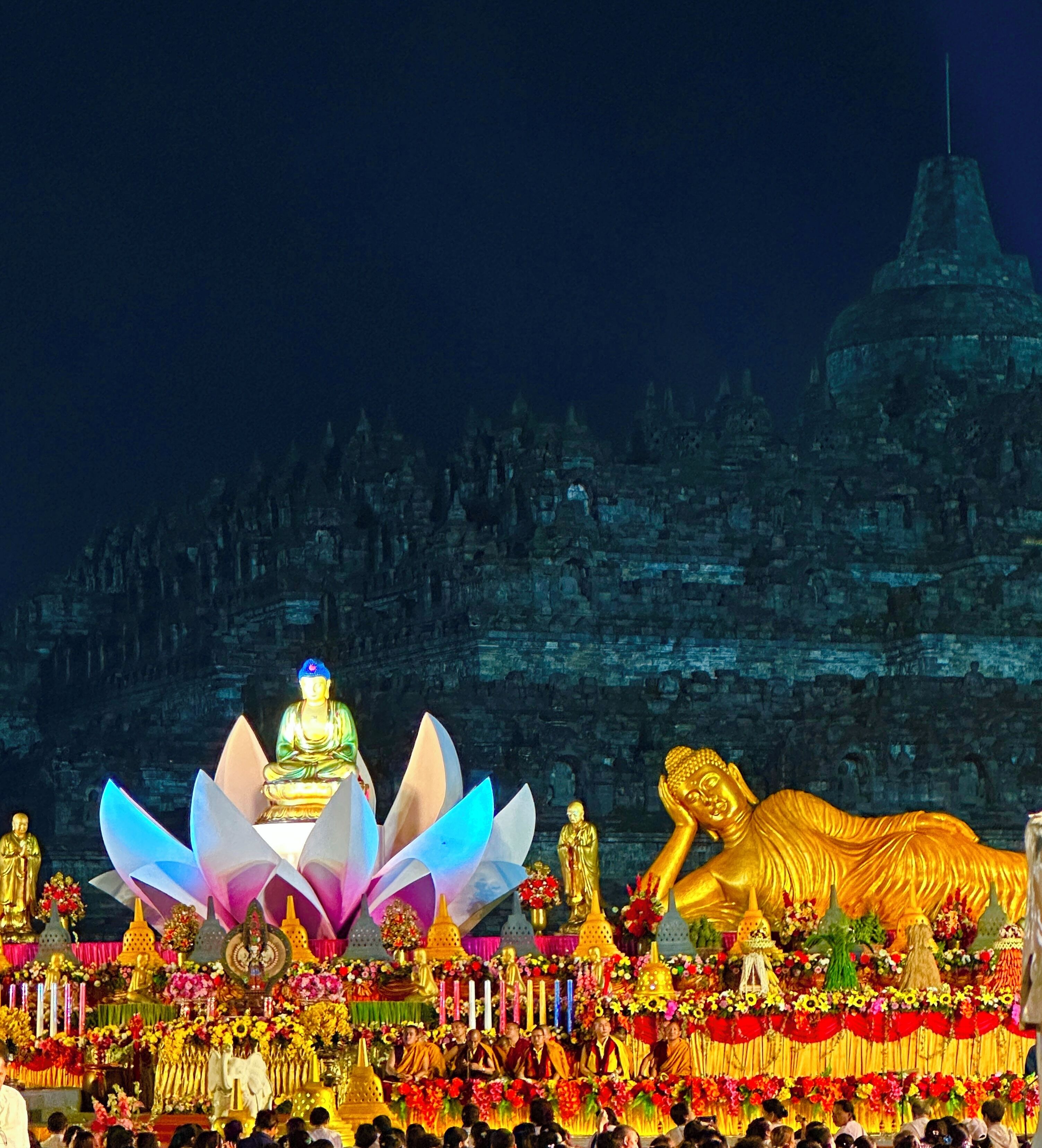 A temple with golden statues and a lotus flower centerpiece, surrounded by a crowd.