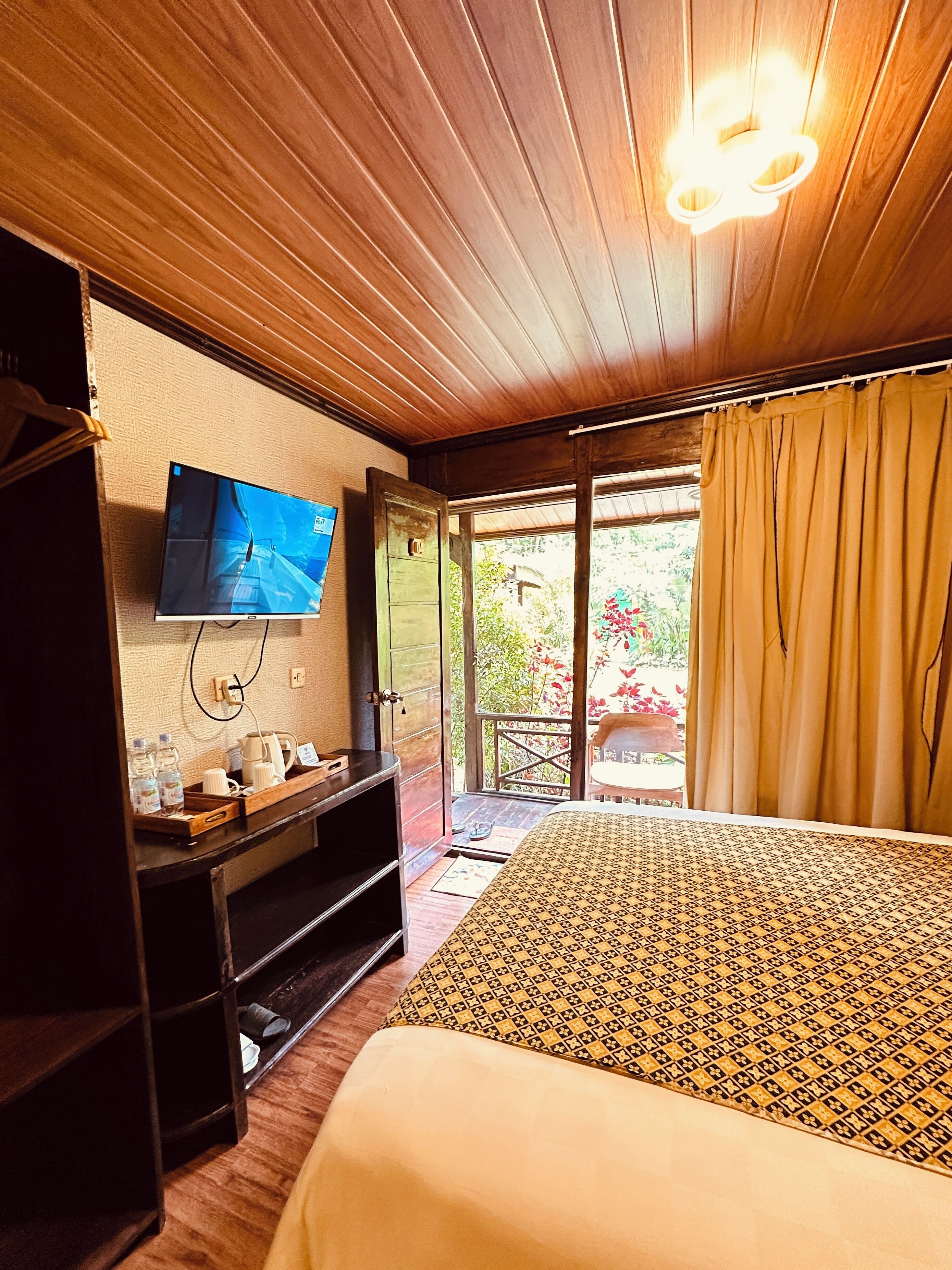 Habitación de hotel con cama, televisor montado en la pared, escritorio de madera con una bandeja de objetos y vista al exterior por una puerta.