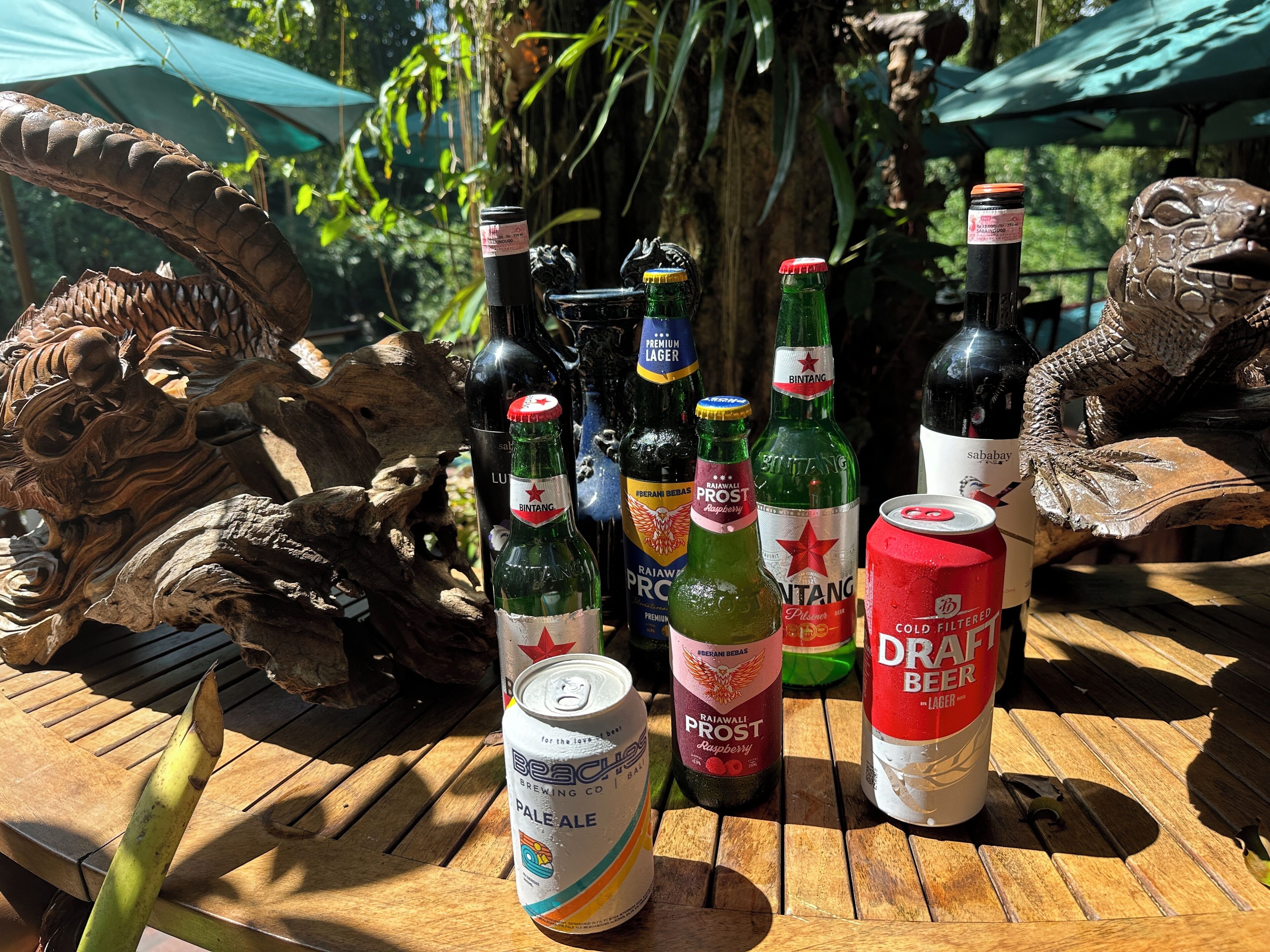 Une table en bois, sur laquelle sont disposées diverses bouteilles et canettes de boissons, le tout entouré de sculptures décoratives en bois.