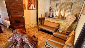 A room with a wooden door, a sofa, a chair, and a large wooden sculpture on the floor.