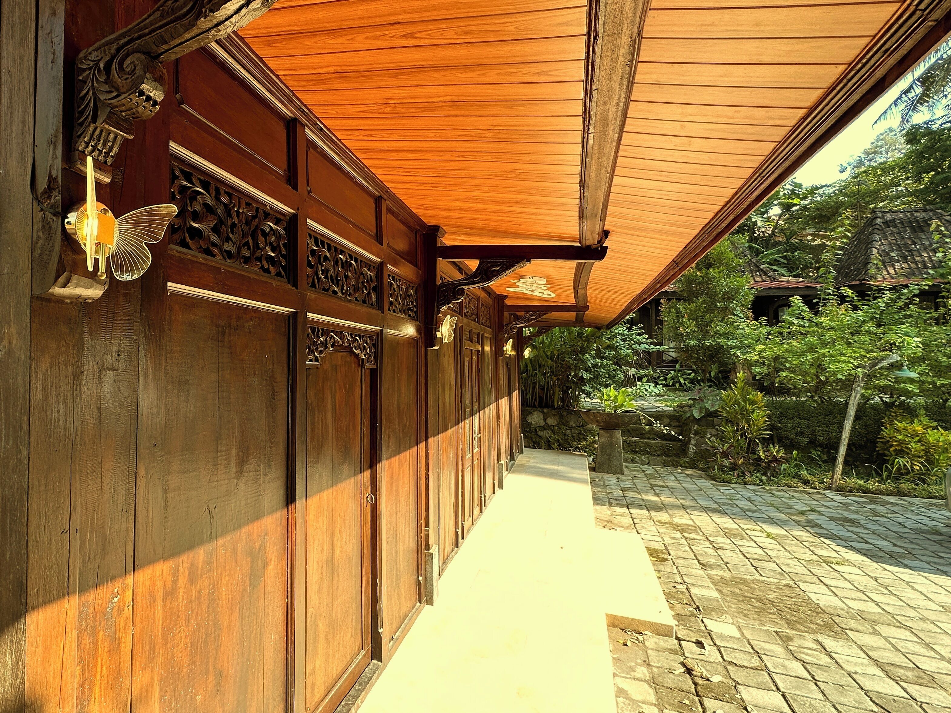 A covered wooden corridor with intricate carvings and a stone pathway leading to a traditional building.