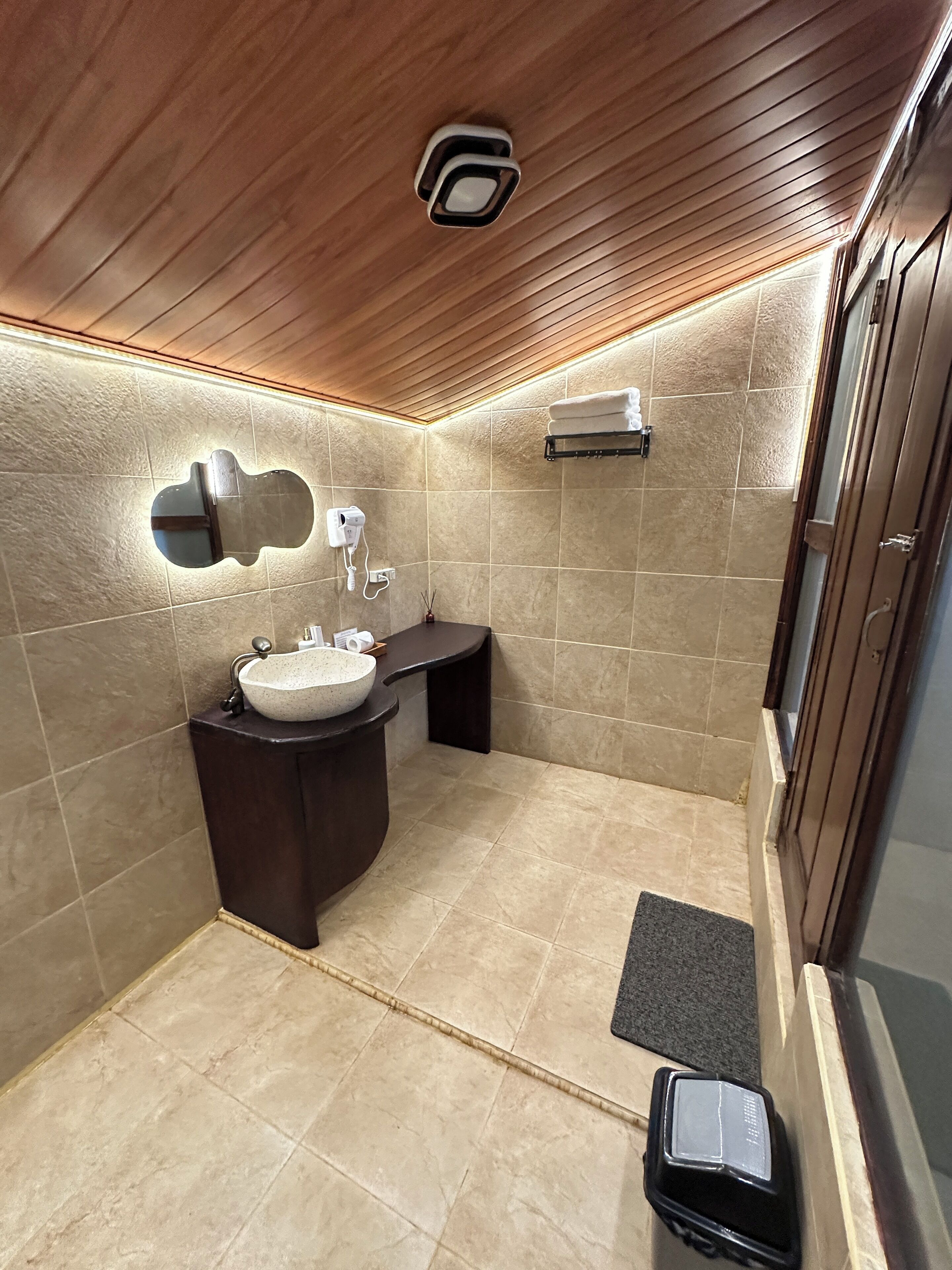 A modern bathroom with a wooden ceiling, a round sink, a towel rack, and a shower area.