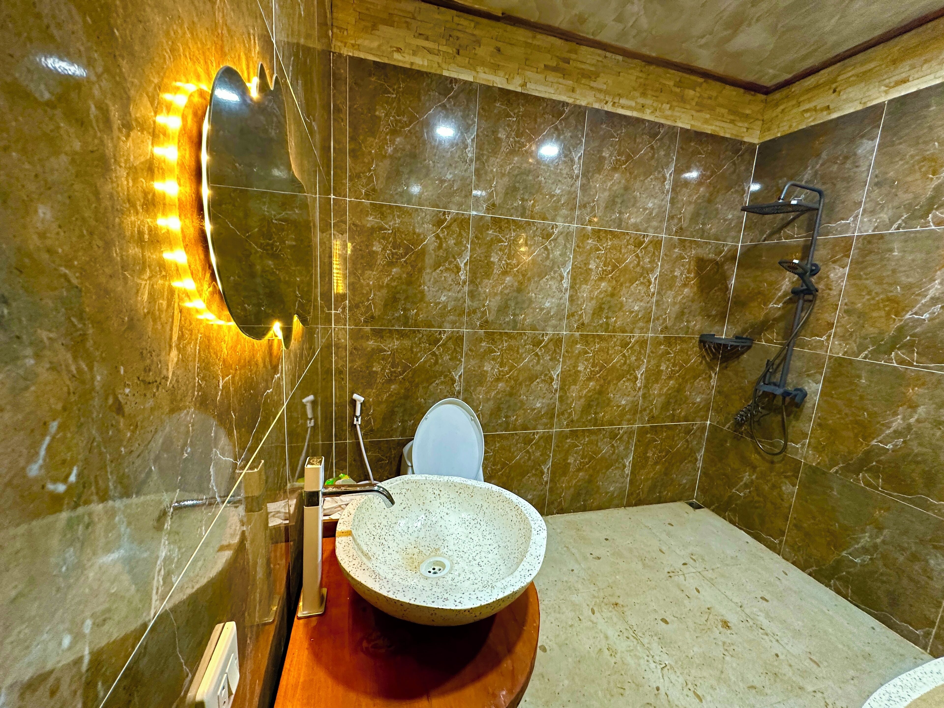 Une salle de bain avec un mur recouvert de carreaux de marbre, un lavabo rond à motifs, un miroir avec éclairage à LED et un espace douche.