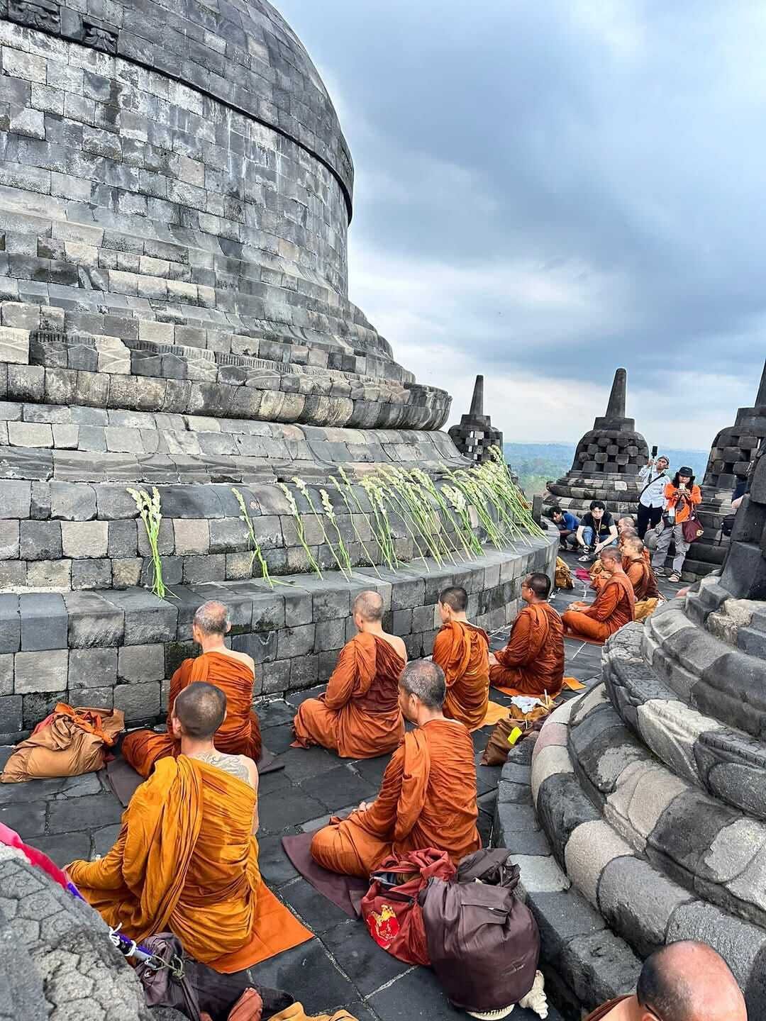 Monks sitting on stone steps in front of a large, curved stone structure.