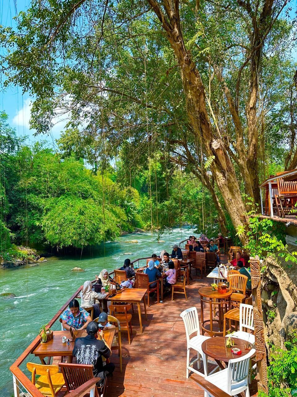 Ein Flussrestaurant mit Außenbereich, das einen Fluss mit Blick auf das sanft fließende Wasser bietet, umgeben von üppiger Vegetation.