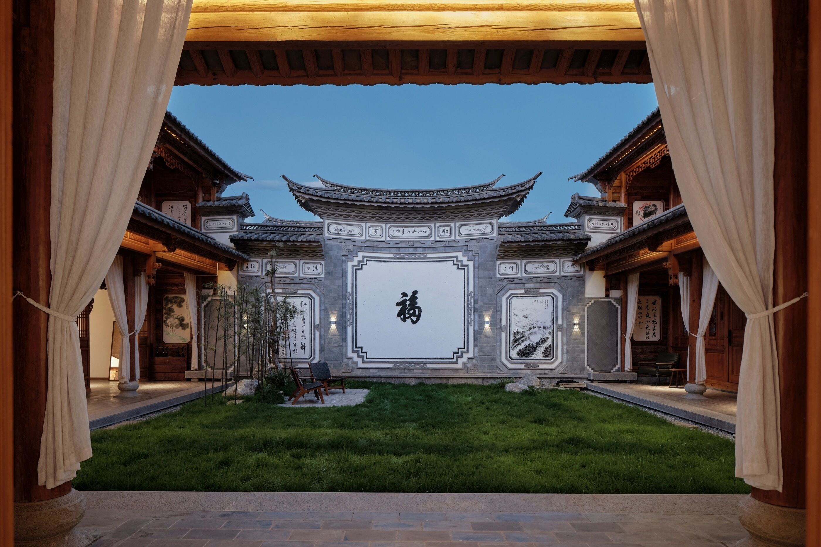 A traditional Chinese courtyard with a central wall featuring calligraphy, surrounded by wooden buildings with tiled roofs.