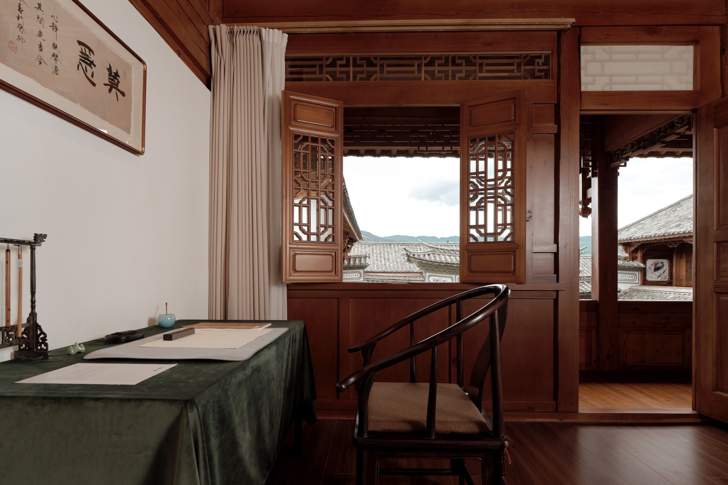 A traditional room with a wooden table, a chair, and a view of traditional architecture through open wooden doors.
