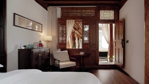 Een hotelkamer met een bed, een stoel, een klein tafeltje, een kast en een raam met gordijnen.