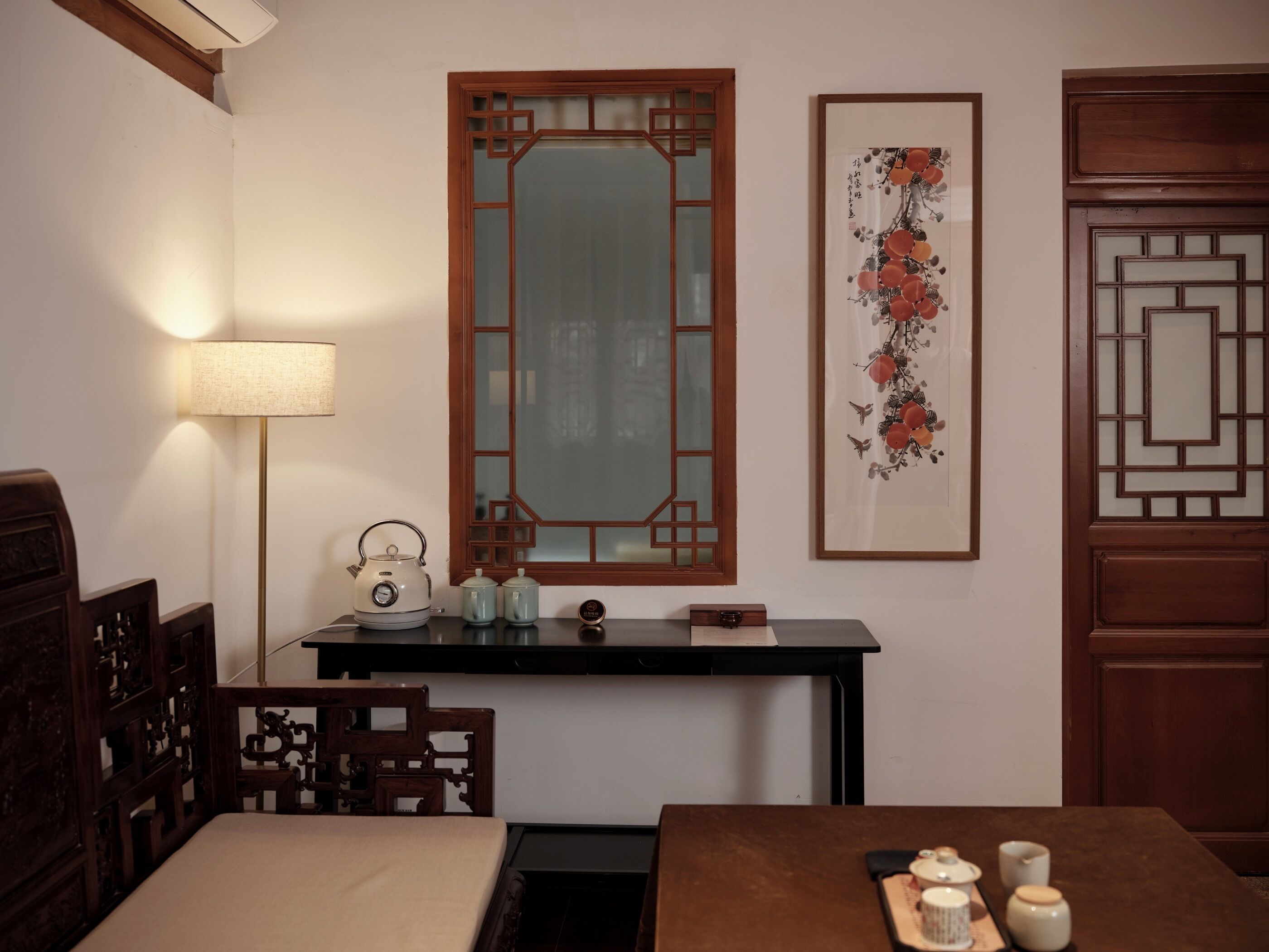 A traditional room with a wooden desk, a tea set, a lamp, and a framed artwork on the wall.