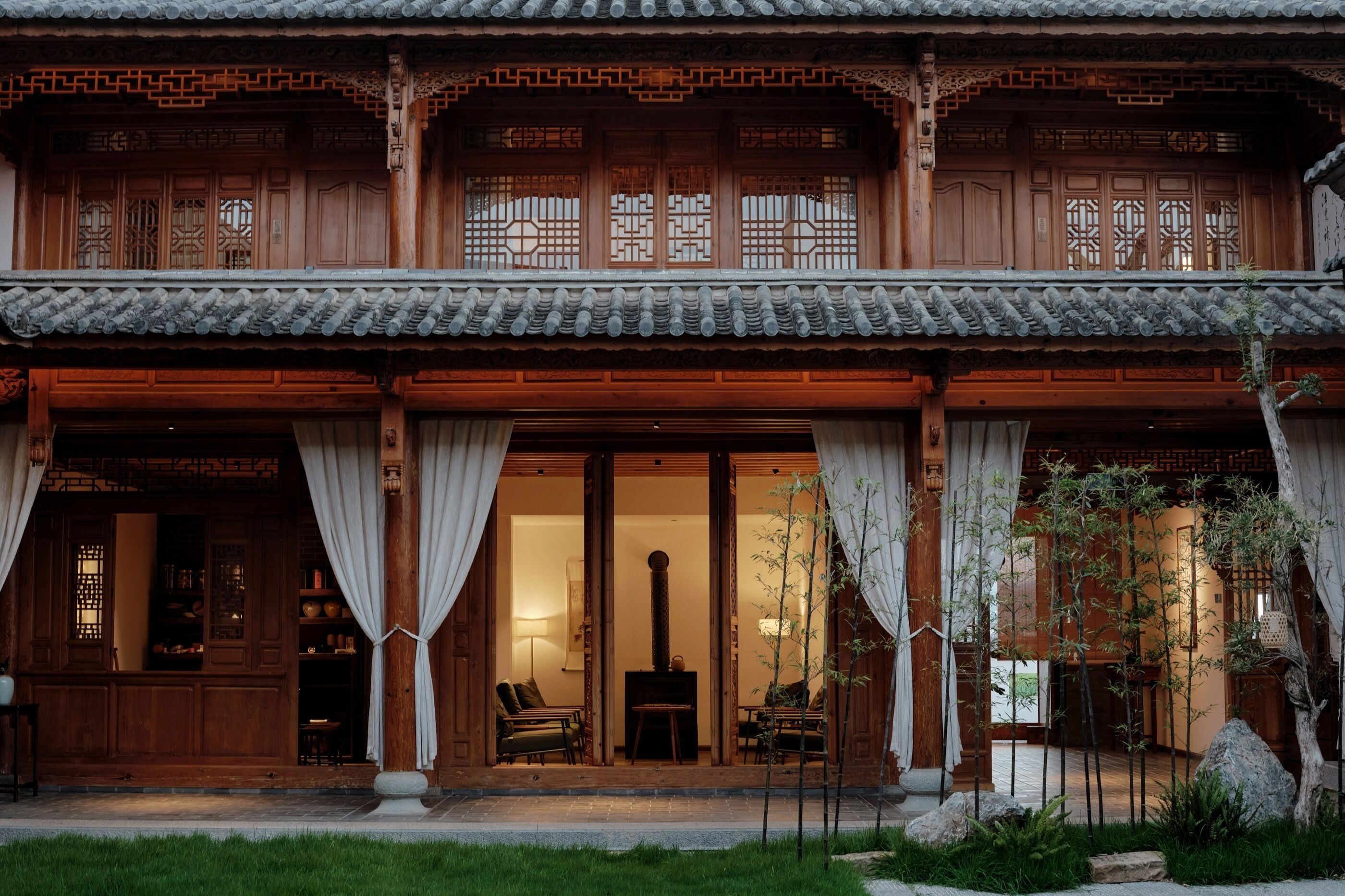 A traditional wooden building with a tiled roof, large wooden doors, and a balcony with curtains.