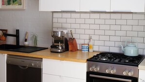 A kitchen with a Bosch dishwasher, a Breville coffee maker, a stove, and a blue kettle on the counter. - Beautiful cottage in the heart of Camperdown! (Camperdown)
