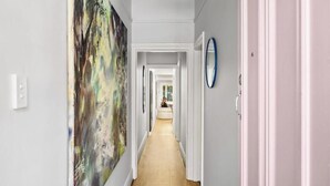A hallway with a large abstract painting on the left, a blue-framed mirror on the right, and a door at the end. - Beautiful cottage in the heart of Camperdown! (Camperdown)