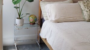 A bedroom with a wooden bed, white bedding, a small white nightstand with a potted plant, and a globe. - Beautiful cottage in the heart of Camperdown! (Camperdown)